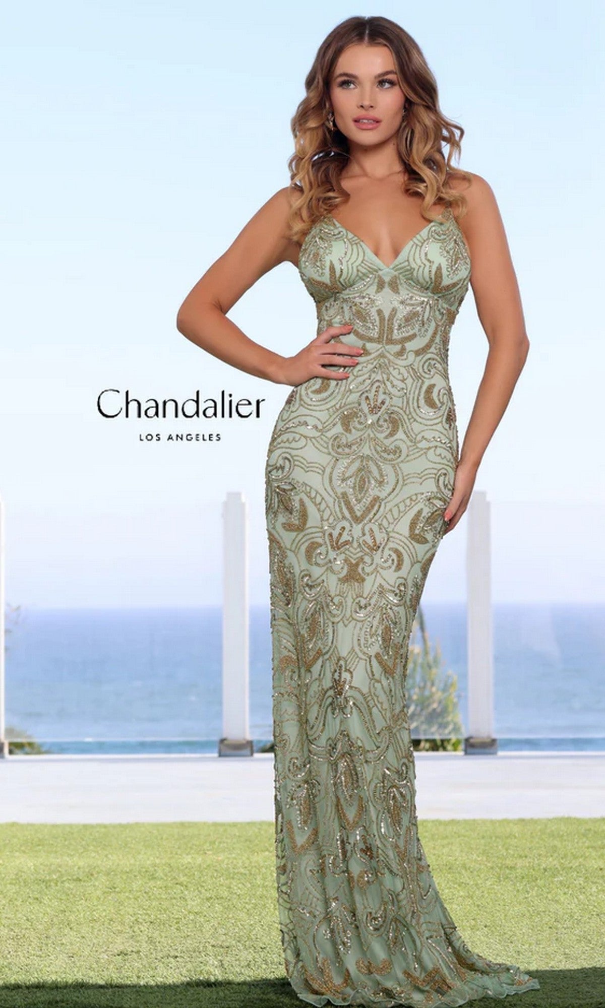 A woman in an aquamarine/gold sequin-print long prom dress (Chandalier 30087) stands on grass with an ocean view behind her.